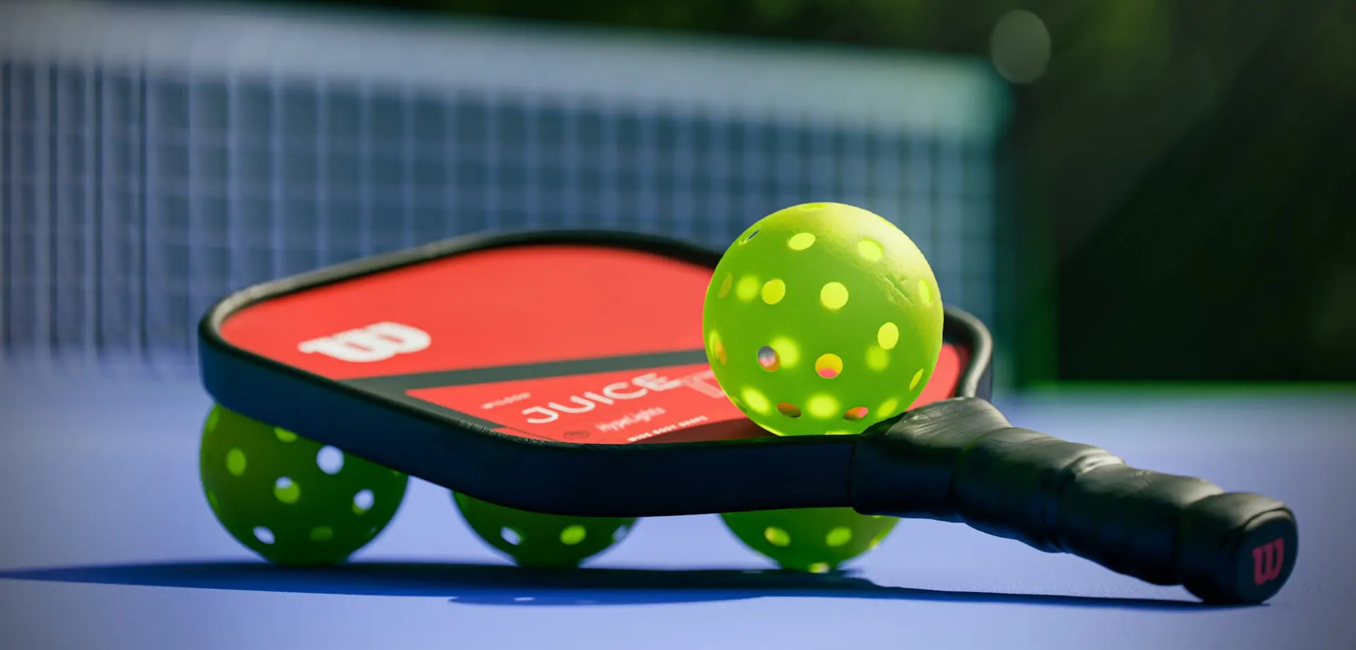 A pickleball paddle and balls on a blue court, in front of the net